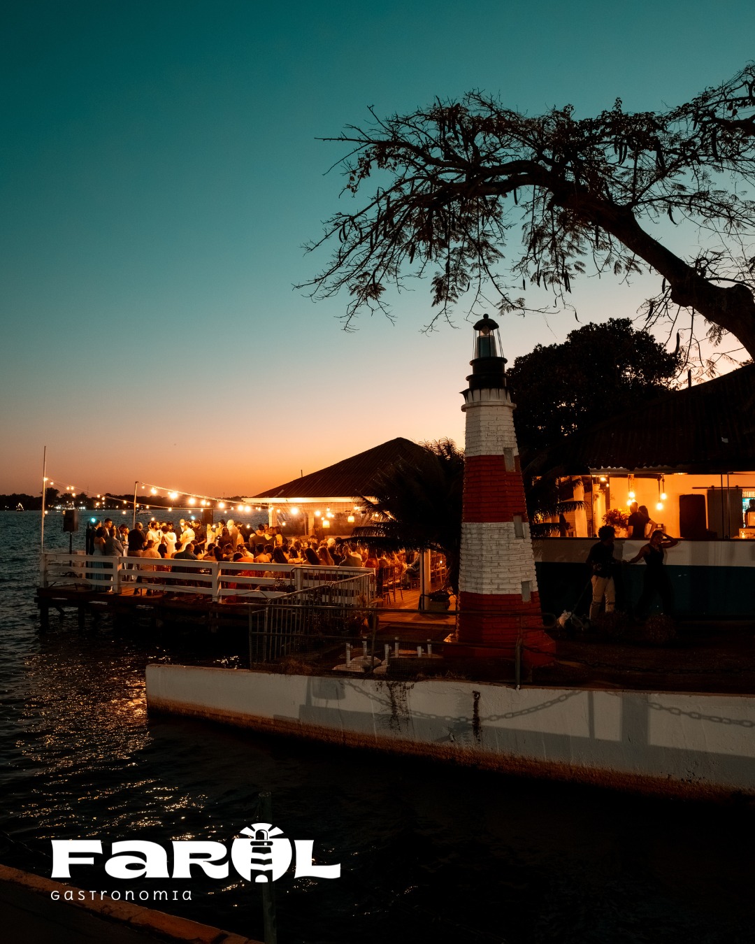 Farol do restaurante iluminado ao entardecer com evento no deck